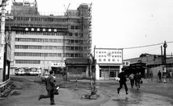 Los personas que van al trabajo se apresuran frente a la Estación Funabashi.En la parte trasera, el Tienda departamental Seibu en ampliación (1970)