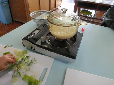 ごはんが見えるなべ。ネギを切っています。