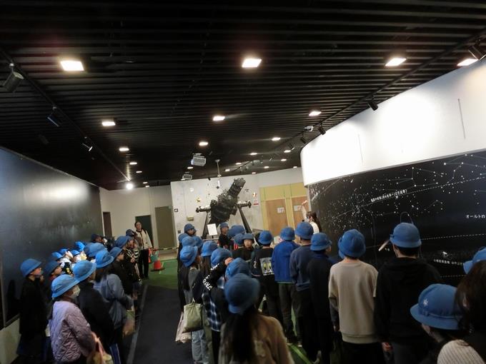 話を聞く子供たちの奥には「コスモくん」が展示されています。